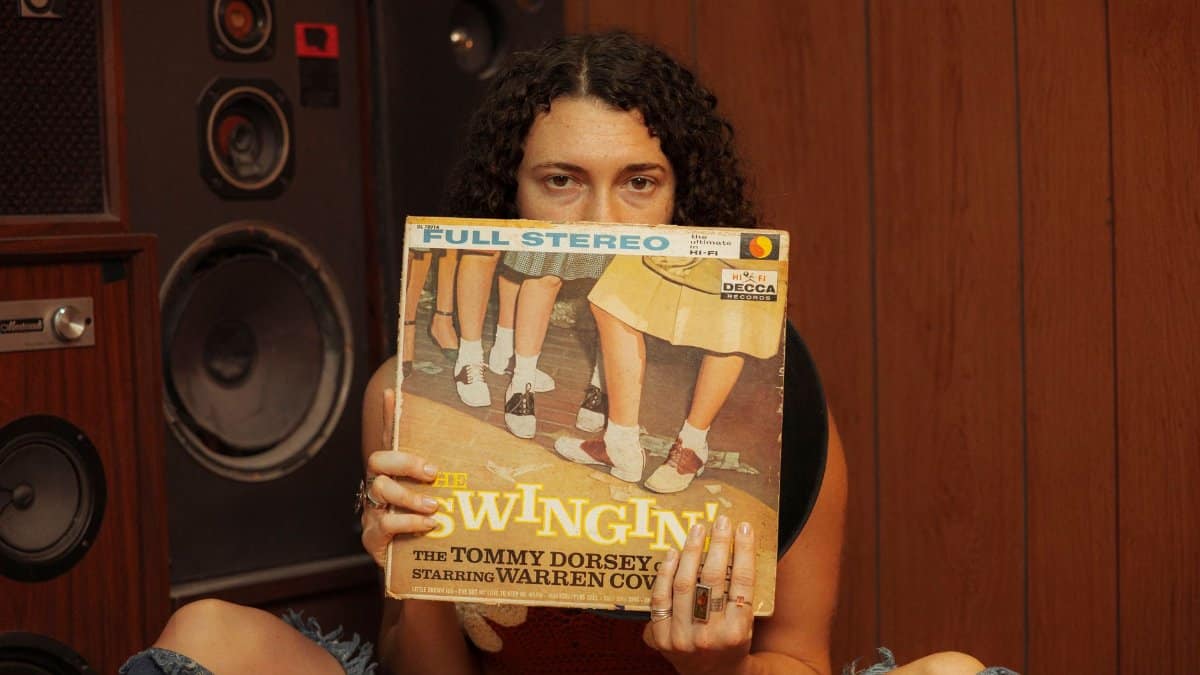 Person holding a vintage vinyl record in front of retro speakers, evoking a classic music ambiance.