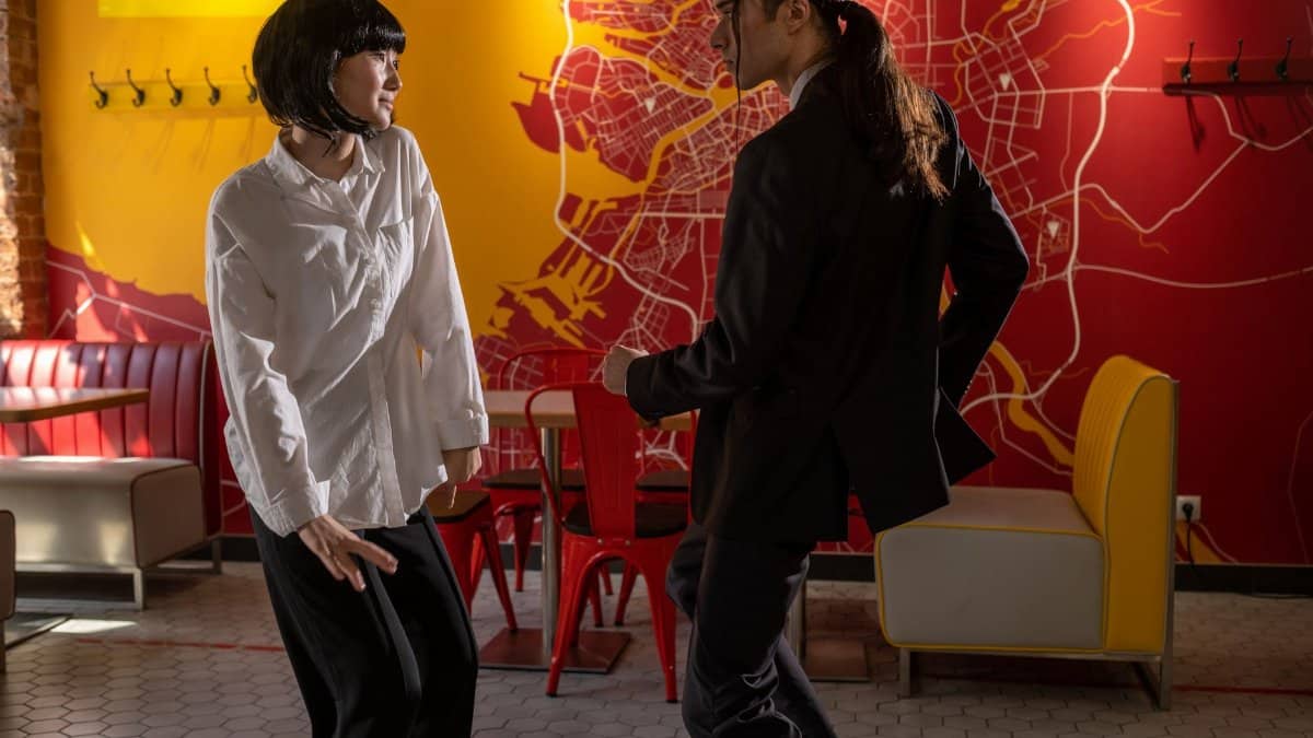 A man and woman dancing joyfully inside a vibrant café with a map-themed wall.