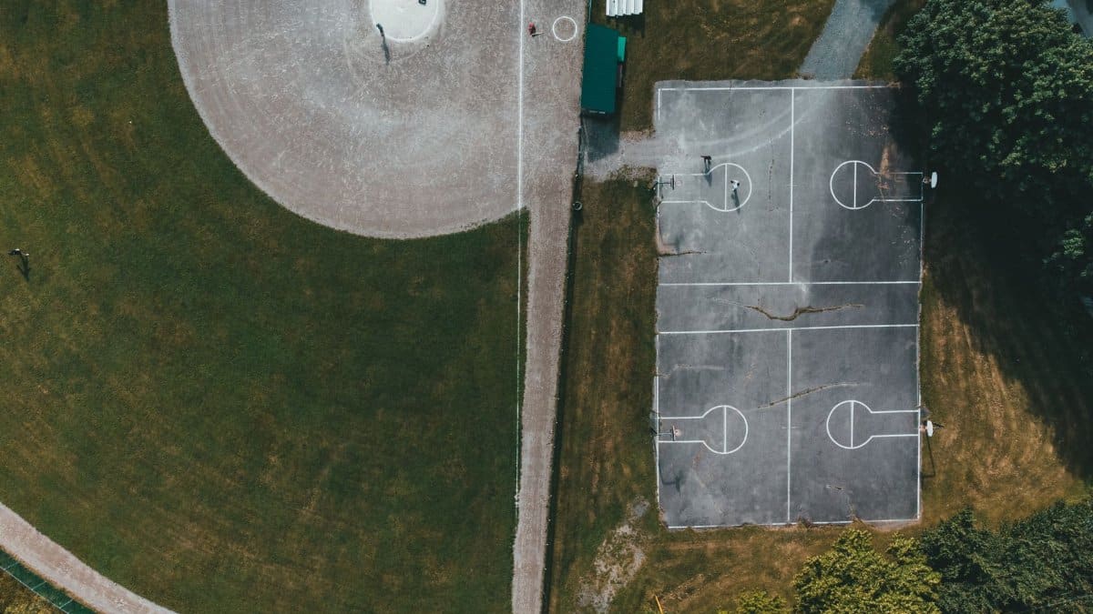 Aerial view of a park featuring a basketball court and baseball field surrounded by greenery.