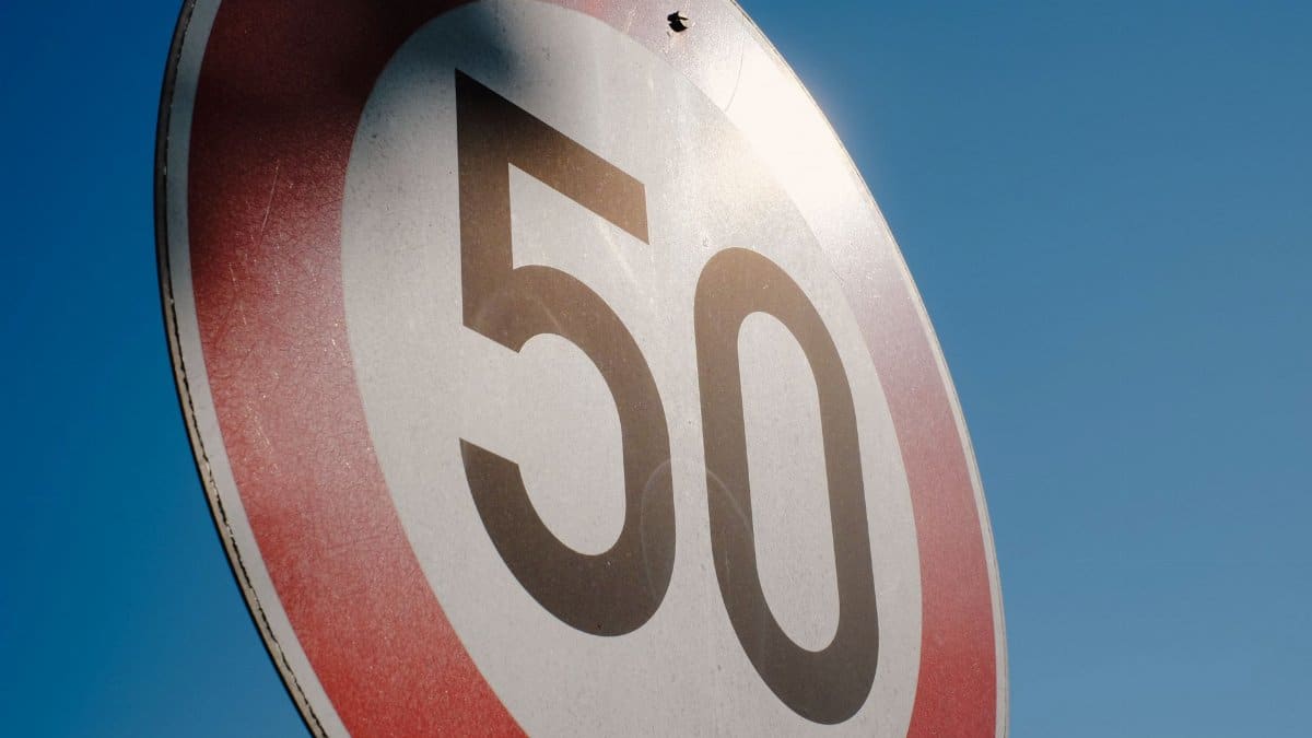 A close-up of a speed limit sign displaying 50 against a clear blue sky backdrop.