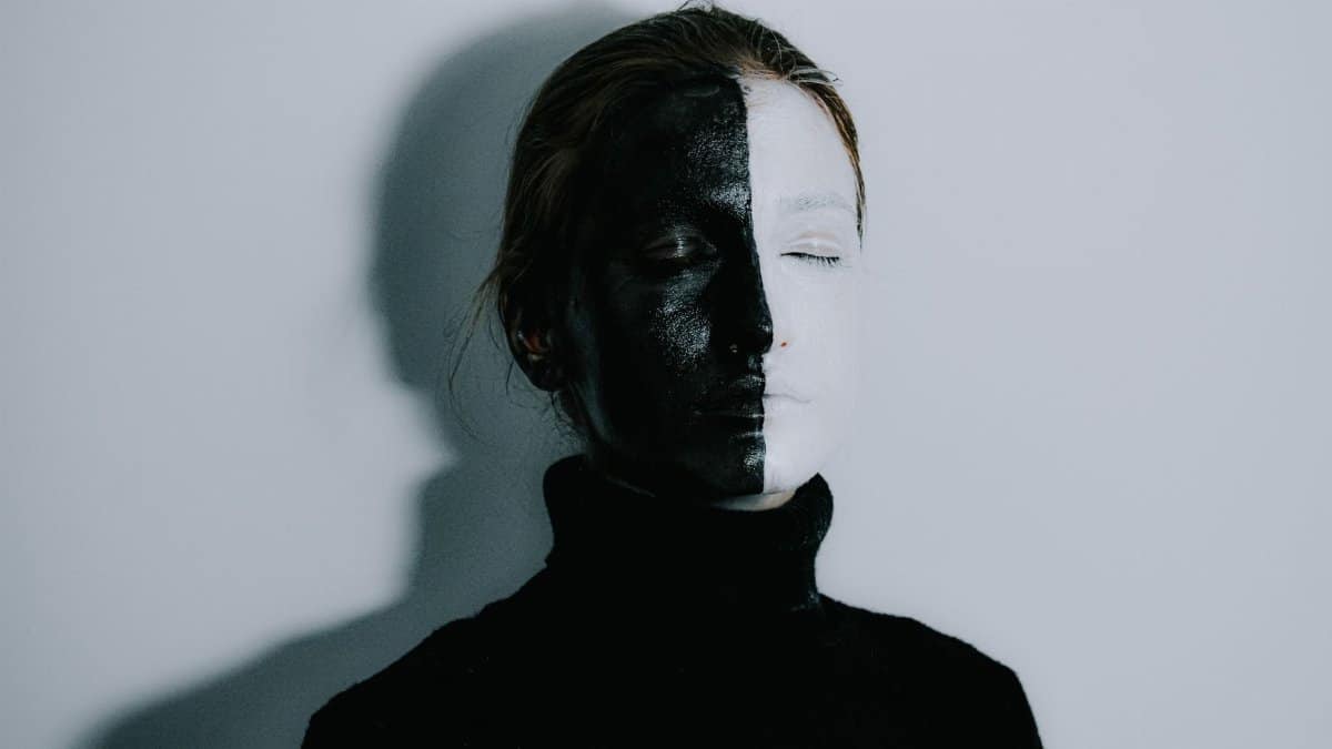 Mysterious female with face painted half in white and half in black colors standing with closed eyes against light background