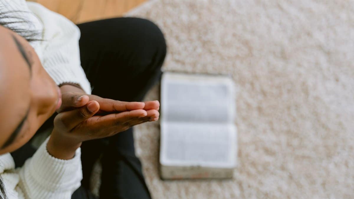 High angle view of a woman in prayer with an open Bible, symbolizing devotion and faith.