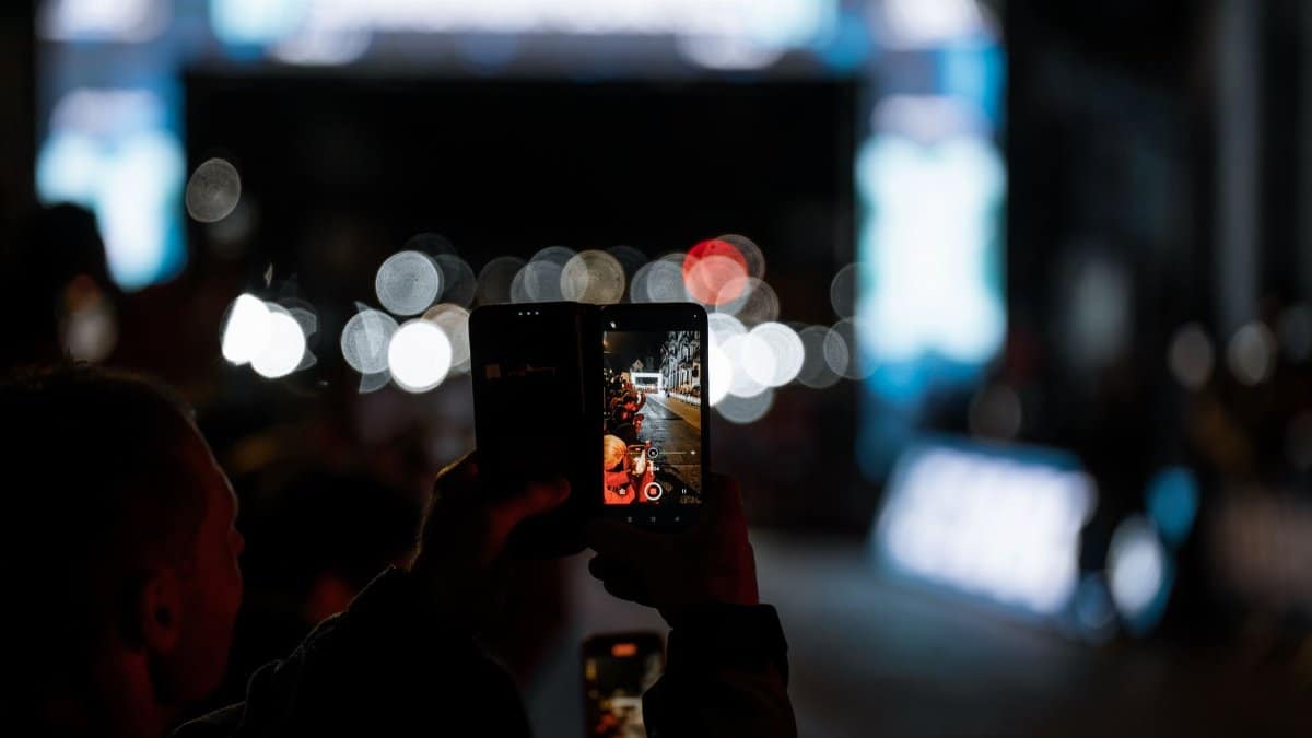 Person photographing an urban scene at night using a smartphone, with vibrant city lights.