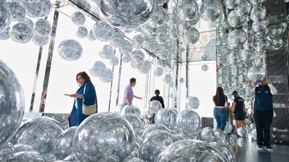 Visitors explore a reflective art installation with mirrored spheres at a New York City observation deck.
