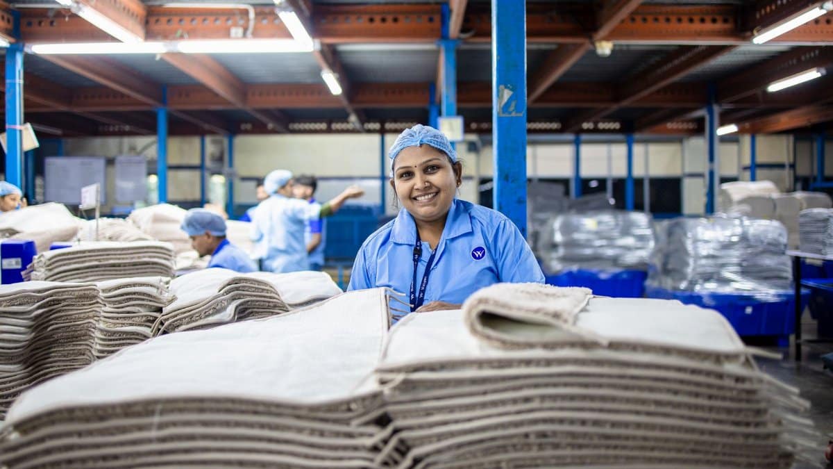 Female worker in a textile factory smiling near stacks of fabric, showcasing blue-collar industry