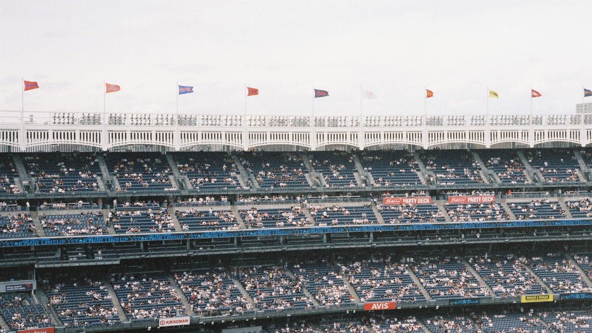 Crowd at Yankee Stadium watching a baseball game, flags waving atop tiers.