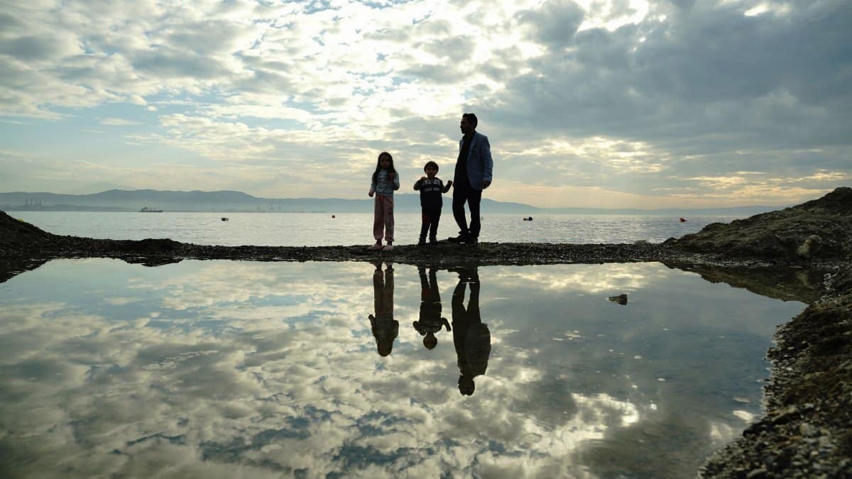 A family standing by water's edge with reflections and dramatic sky in Bursa.