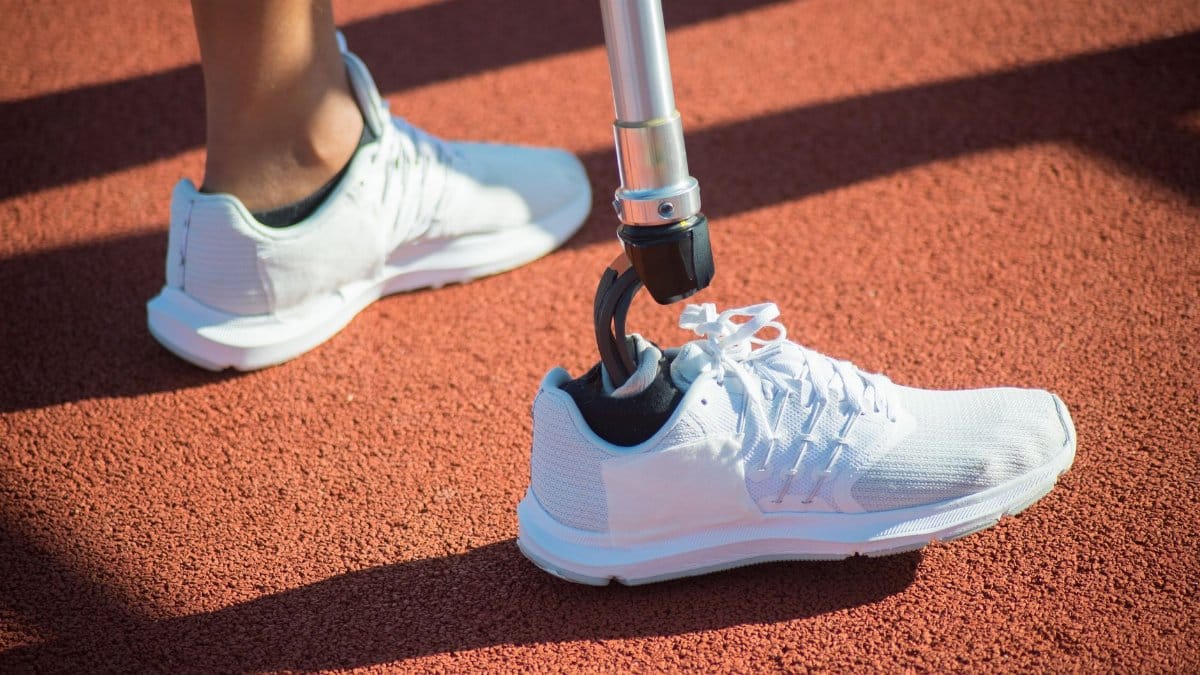 Close-up of a prosthetic leg wearing white sneakers on a sunny track, emphasizing athletic resilience.