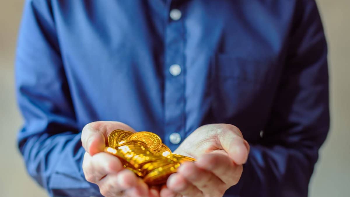 A person in a blue shirt holds a handful of shiny golden coins, symbolizing wealth and cryptocurrency.