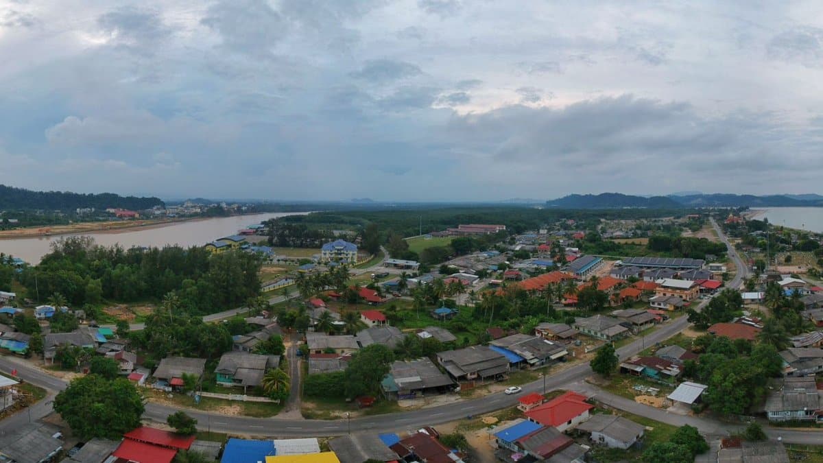A panoramic aerial view of a coastal village with diverse landscapes, trees, and houses.