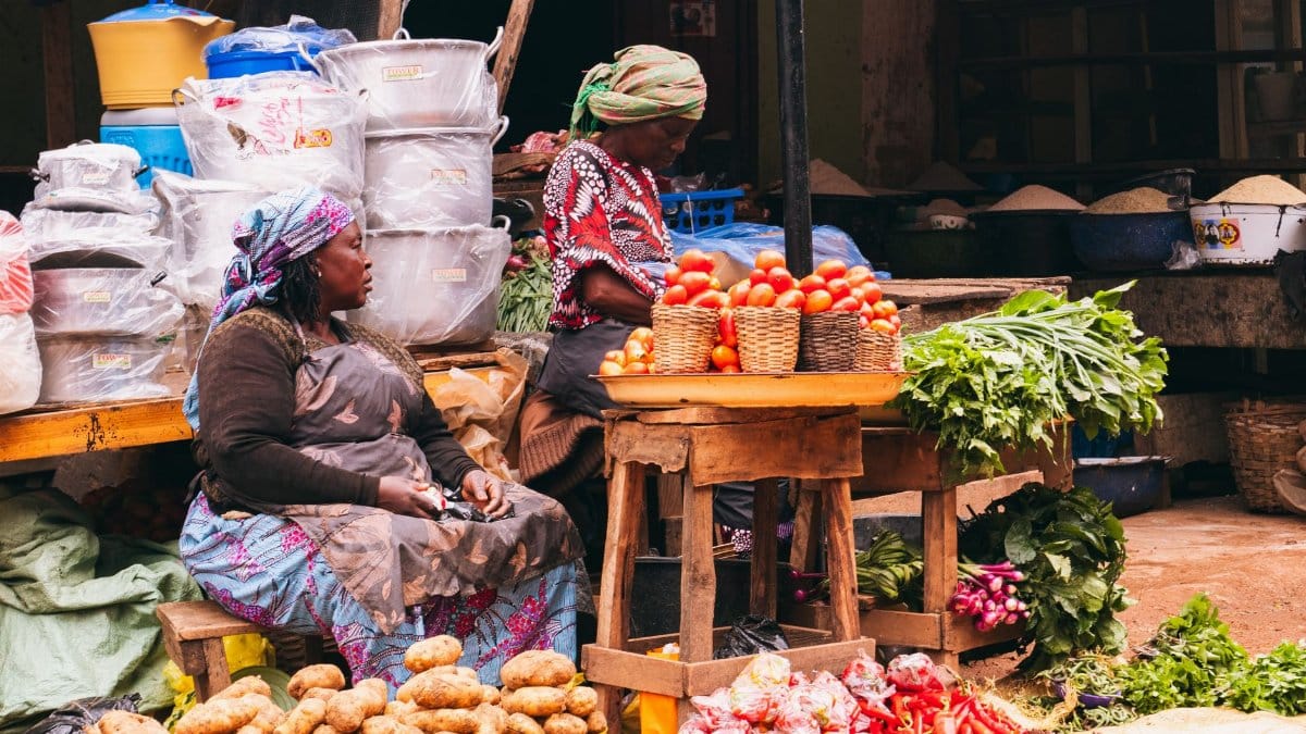 Colorful market scene in Jos, Nigeria showcasing women selling fresh produce with vibrant vegetables and baskets.