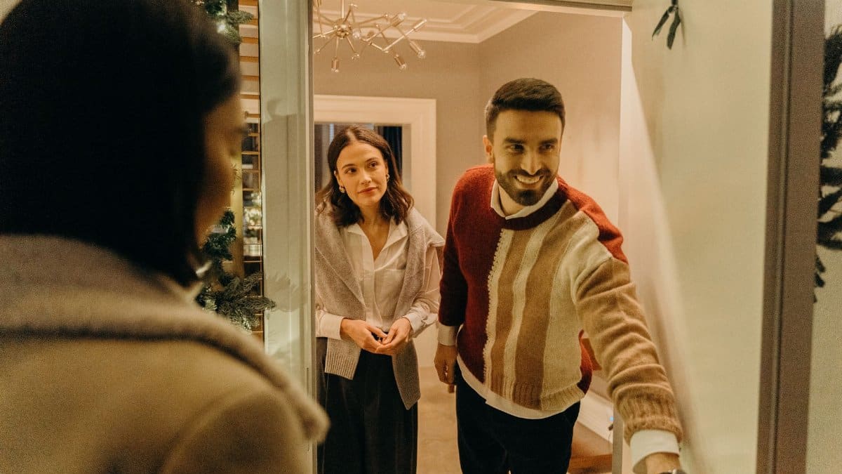 A couple greeting a guest at their doorway, capturing the warmth of a home during the holiday season.