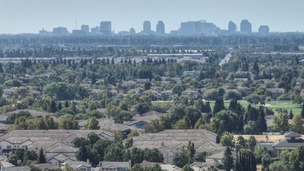 Aerial view of Sacramento's suburban homes with the city skyline in the distance. Lush greenery and clear skies.