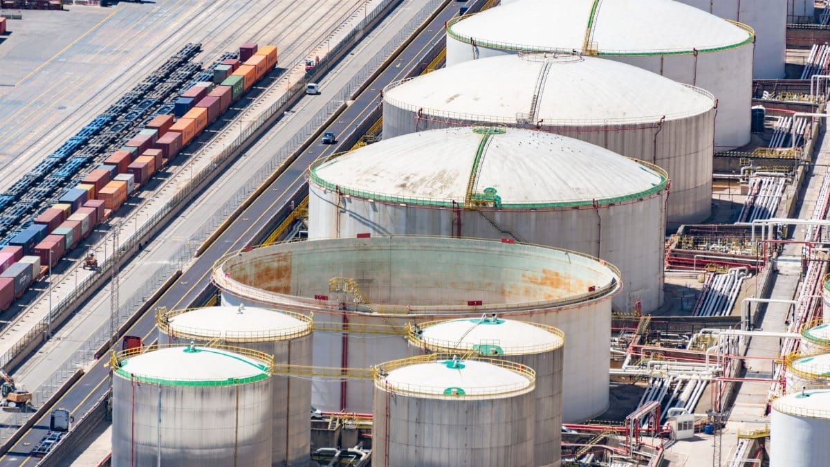 Aerial shot of large oil storage tanks in an industrial district with adjacent railway tracks.