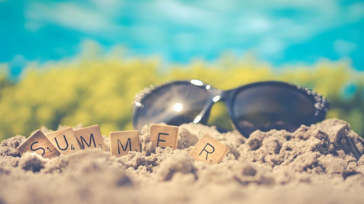 Sandy beach scene with sunglasses and 'summer' spelled in letter tiles, capturing vacation vibes.