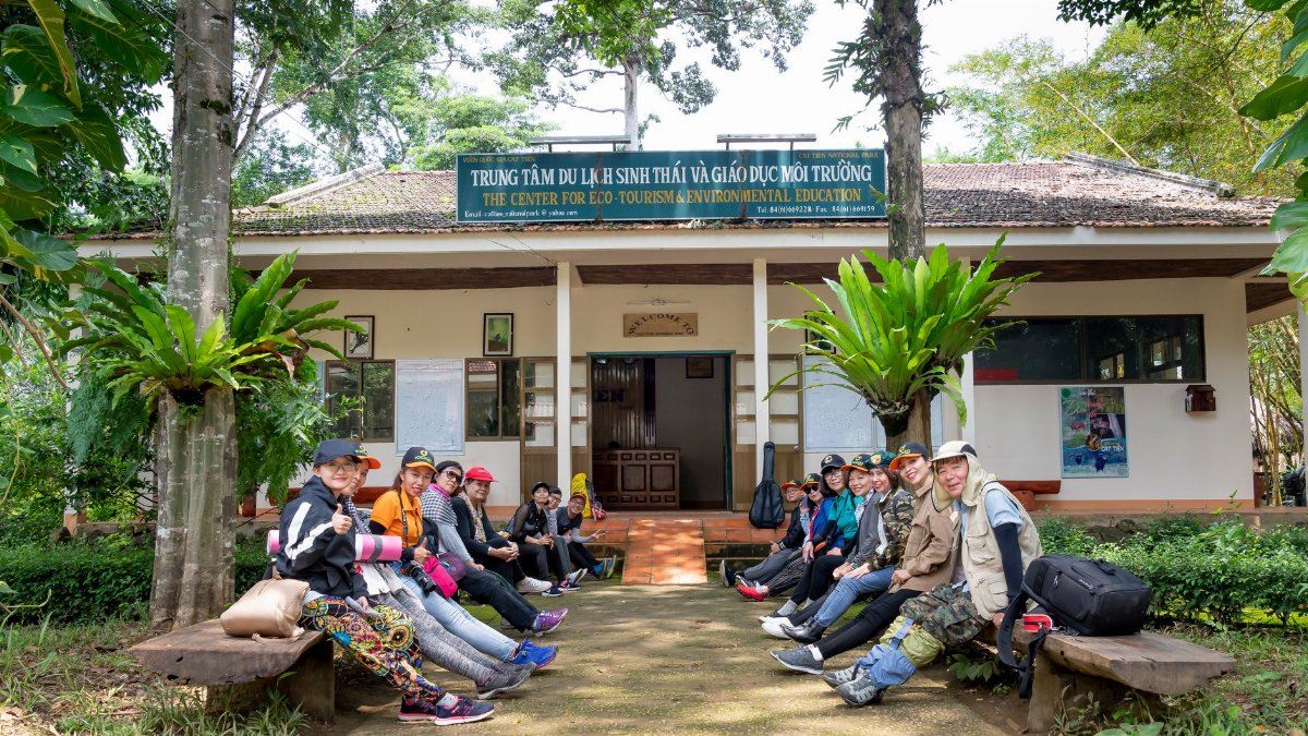 Team of travelers with backpacks waiting for start of trekking excursion while sitting near entrance of tourist agency