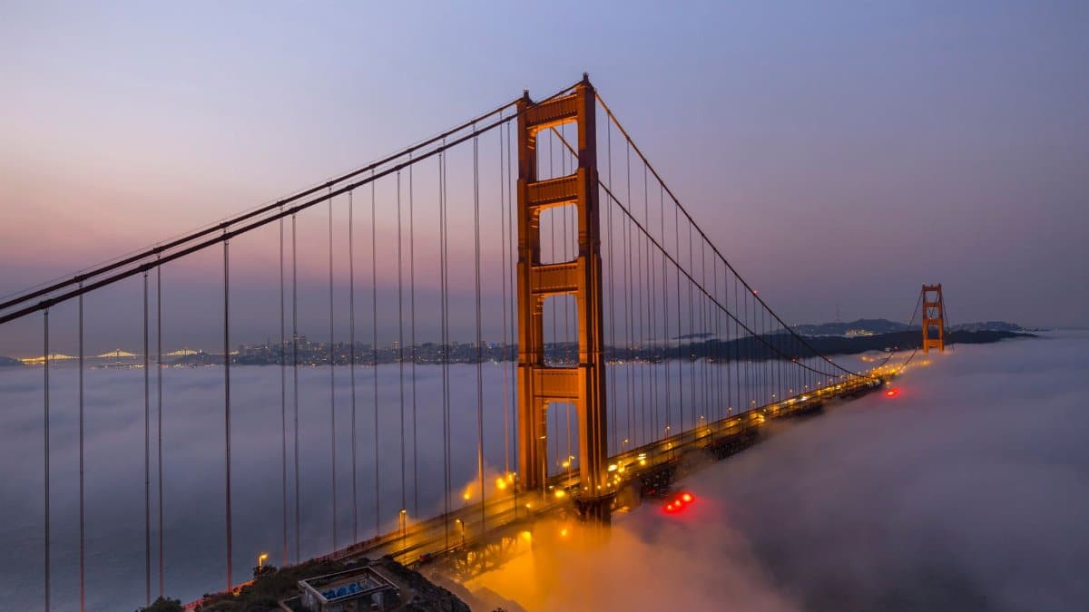 Golden Gate Bridge enveloped in morning fog under a colorful dawn sky.