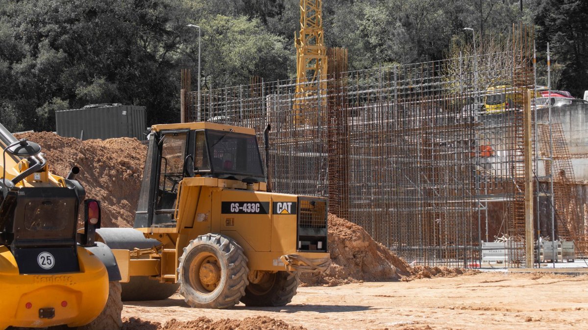 Yellow construction machinery and steel framework on a large active construction site outdoors.