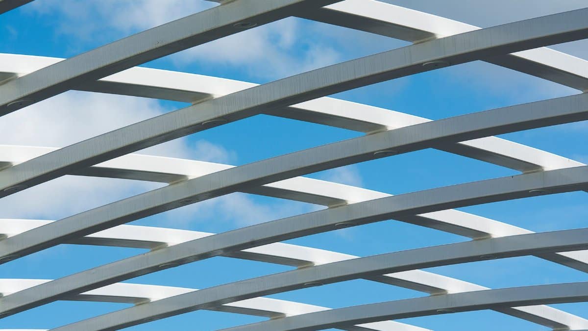 Sleek white steel beams form a modern geometric pattern against a bright blue sky.