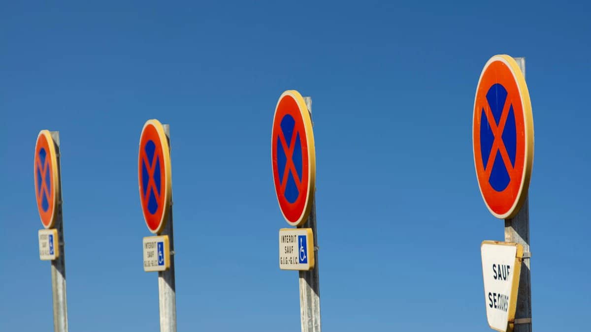 Four no parking traffic signs aligned under a clear blue sky, taken outdoors.