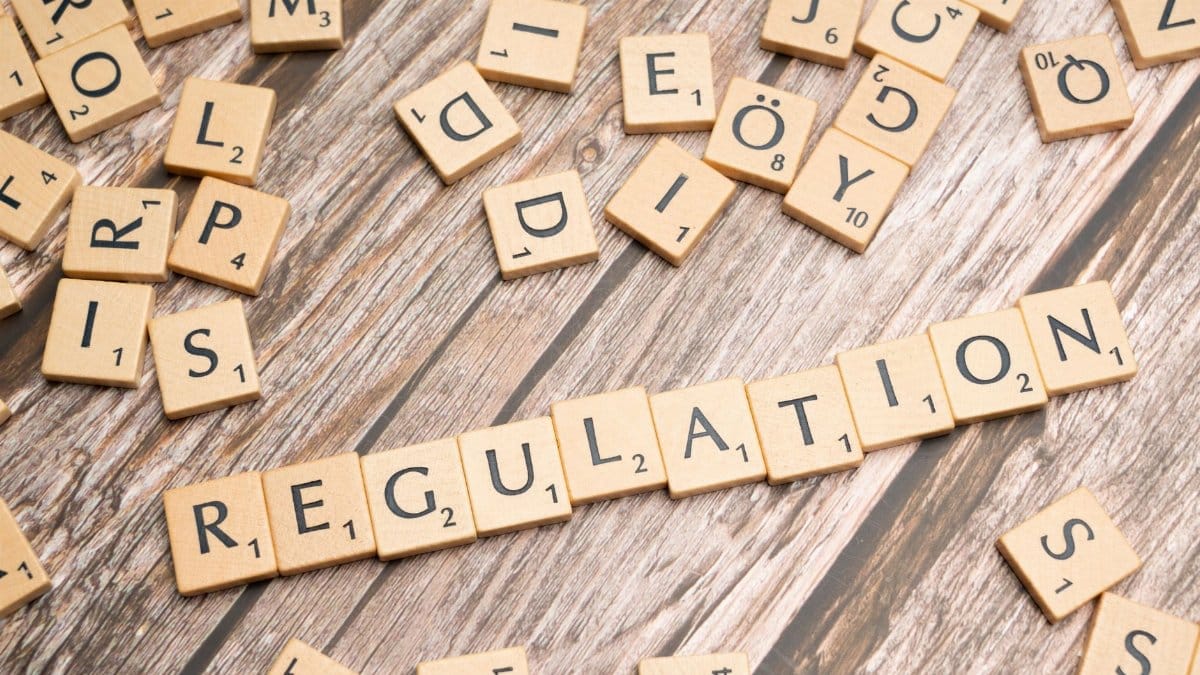 Wooden letter tiles spelling 'Regulation' on a textured wood background, conveying themes of compliance and structure.