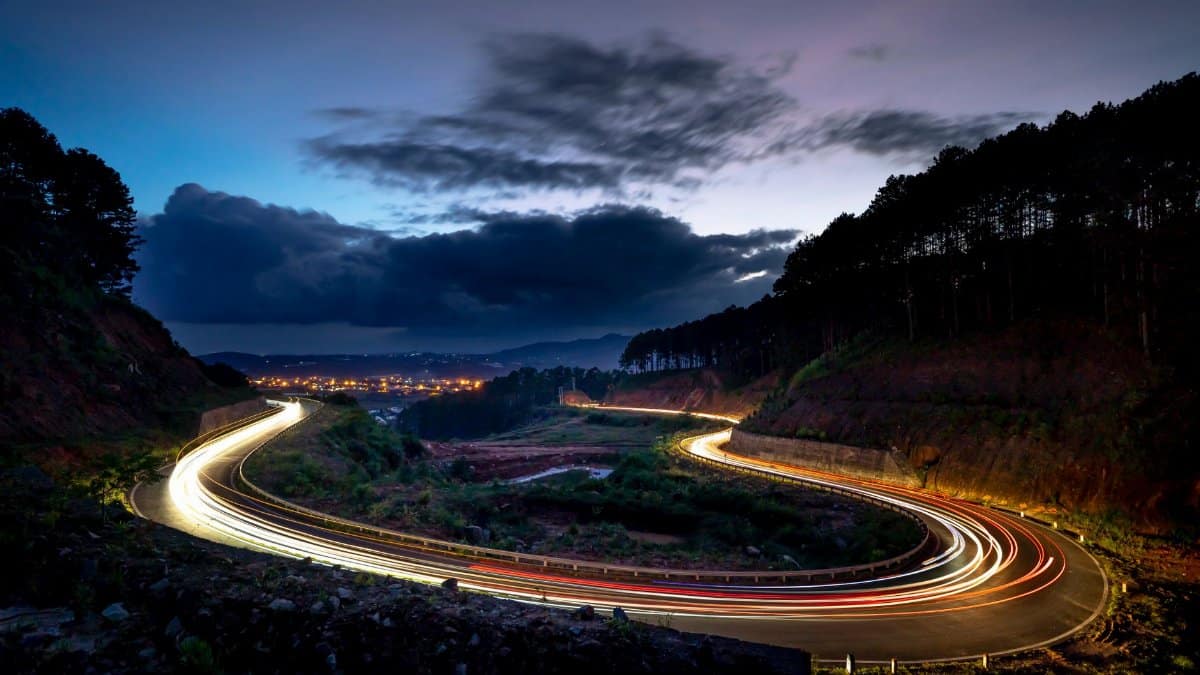 Captivating long exposure of a winding road at twilight with vivid light trails and a scenic landscape.