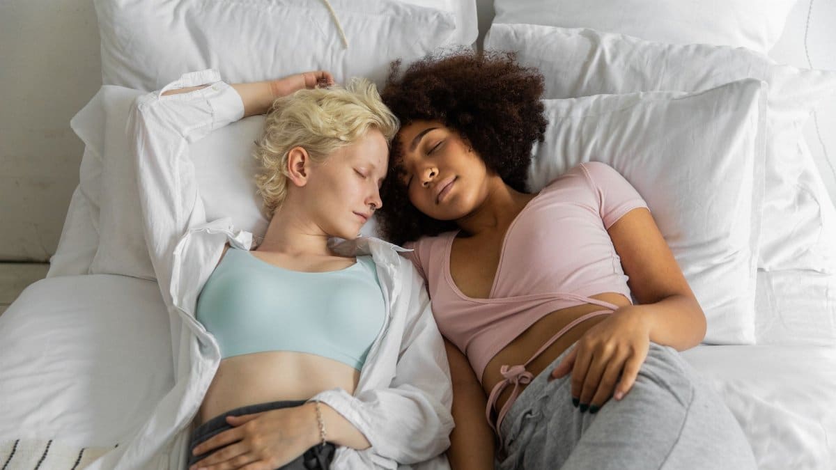 From above of peaceful multiracial homosexual couple lying close during sleep at weekend in cozy room
