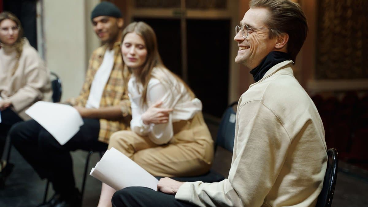 A group of actors smiles during a theater rehearsal session indoors.