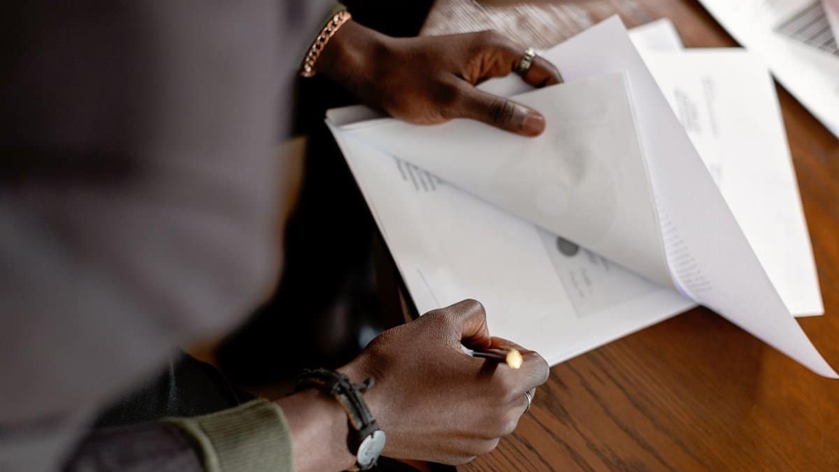African American adult revising papers with a pencil at a desk, focus on hands and documents.