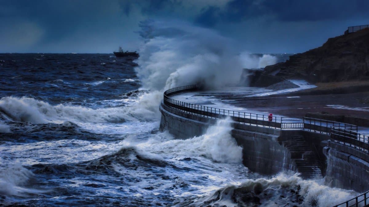 Powerful ocean waves crash against a concrete seawall during a storm.