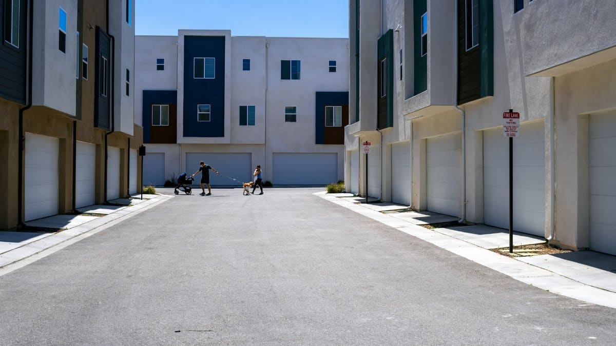 A quiet urban alley framed by sleek modern residential buildings under a summer sky.