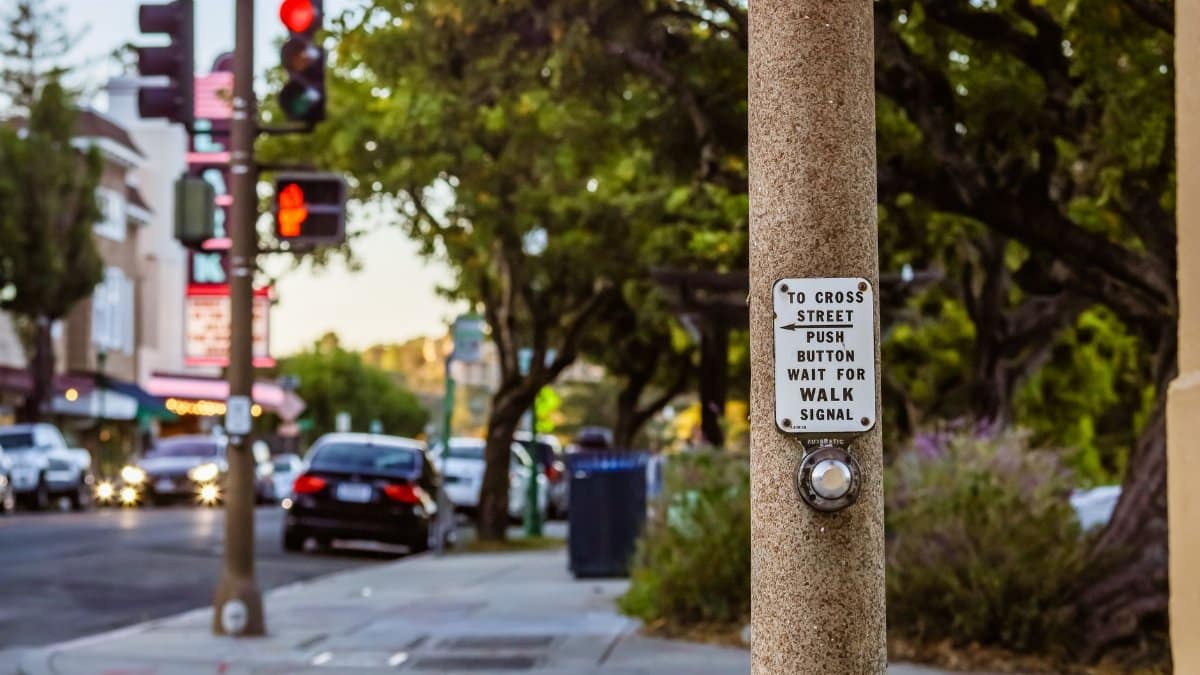 City street featuring a pedestrian crossing signal button and urban surroundings.