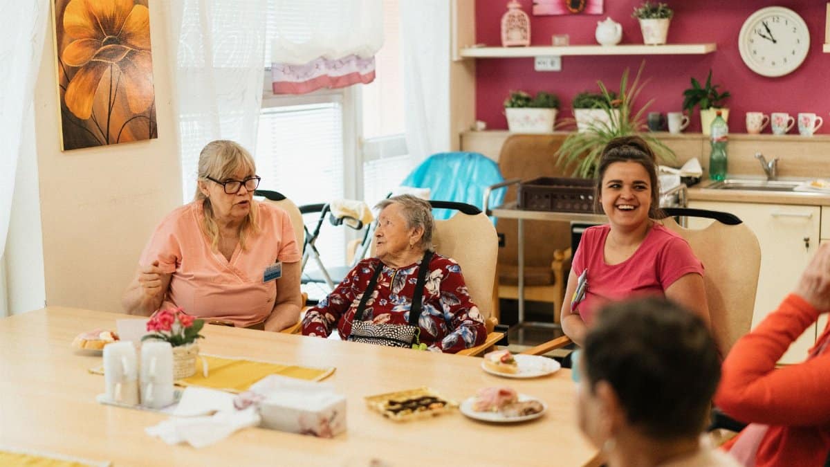 Elderly residents and caregivers enjoying a meal and conversation in a cheerful dining space.