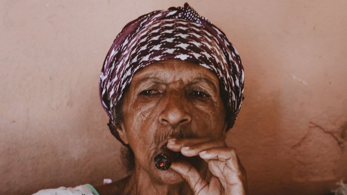 An elderly woman wearing a headscarf smokes a cigar, showcasing cultural traditions and expressions.