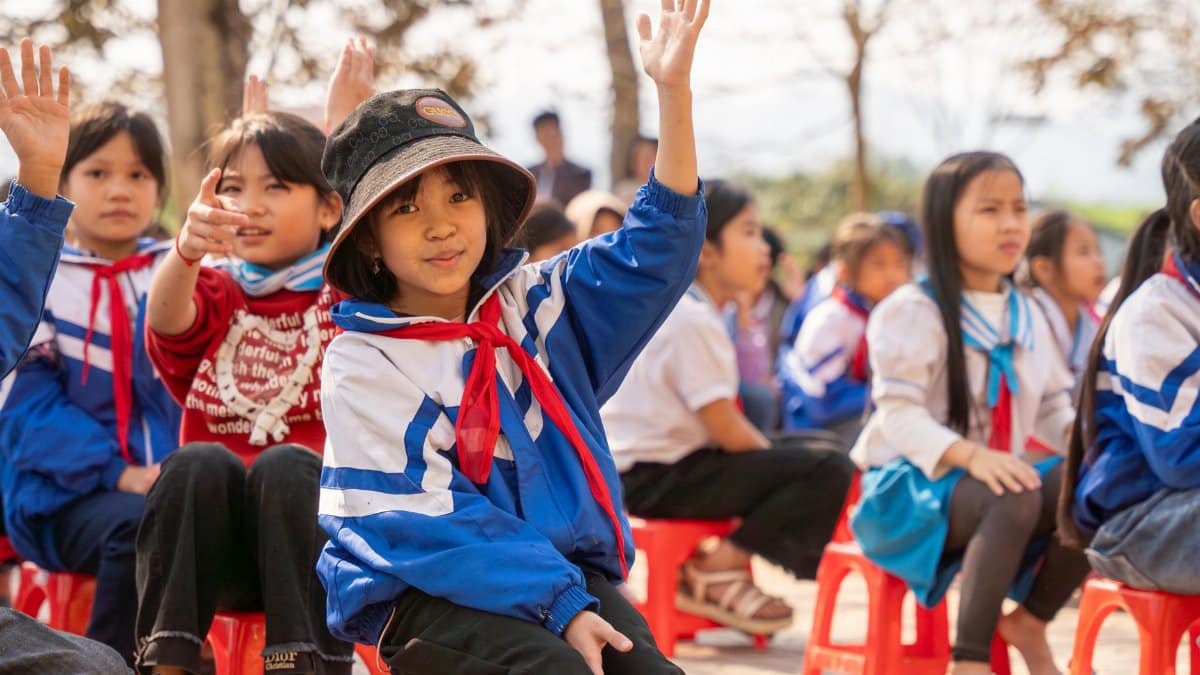 Children in uniforms raising hands outdoors, enjoying a fun educational activity in a park setting.