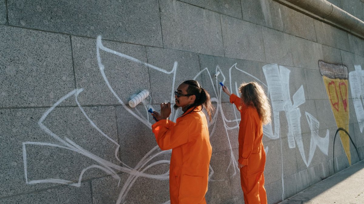 Two individuals cleaning graffiti from a concrete wall in an urban area.