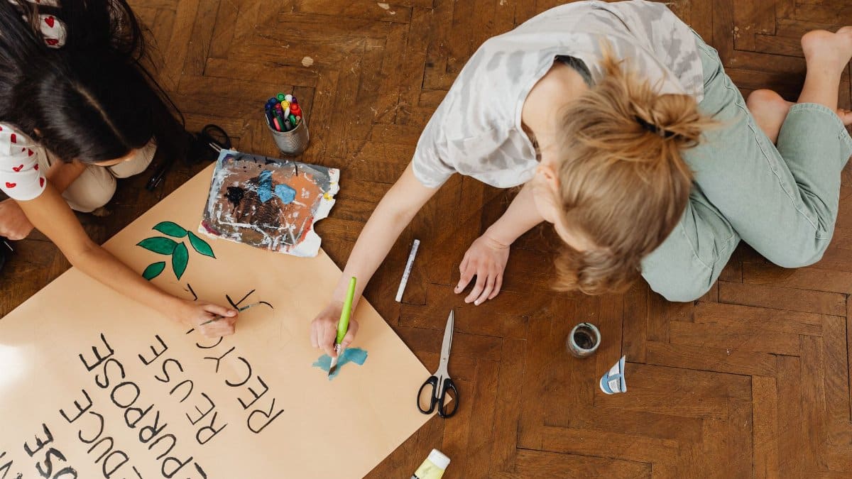 Two teenagers work together on a recycling themed school project indoors.