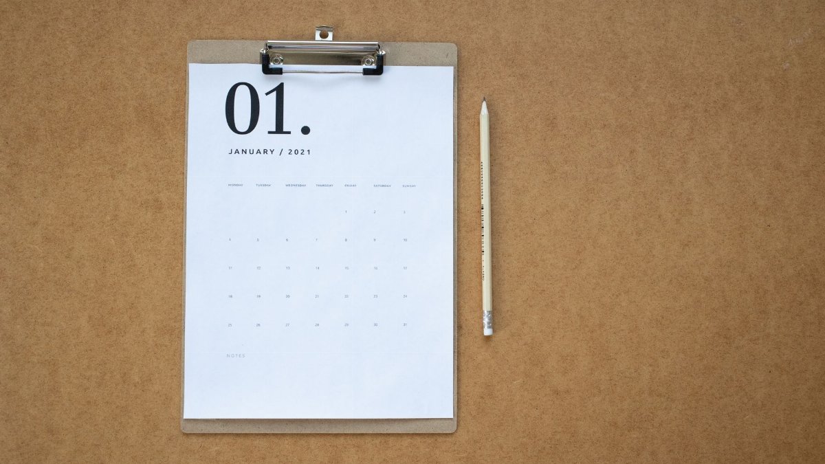 Flat lay of a January 2021 calendar on a clipboard with a pencil on brown background.