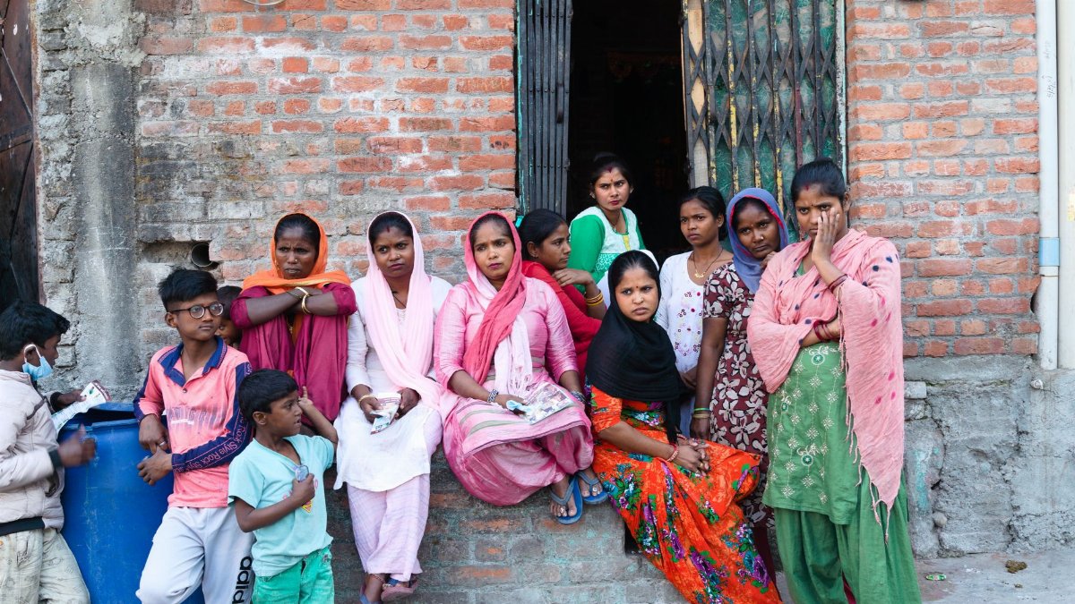 A vibrant group sits outside a brick house in rural Haldwani, India, showcasing local lifestyle.