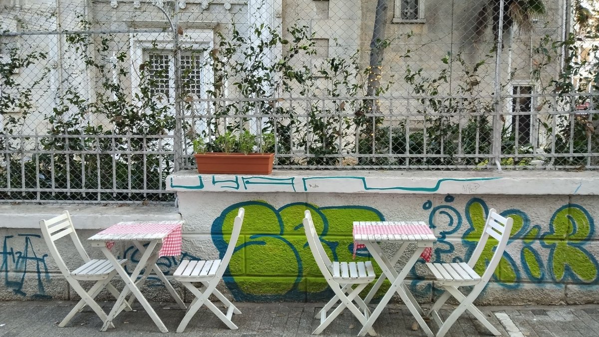 Outdoor café scene with white tables and chairs, urban graffiti art.