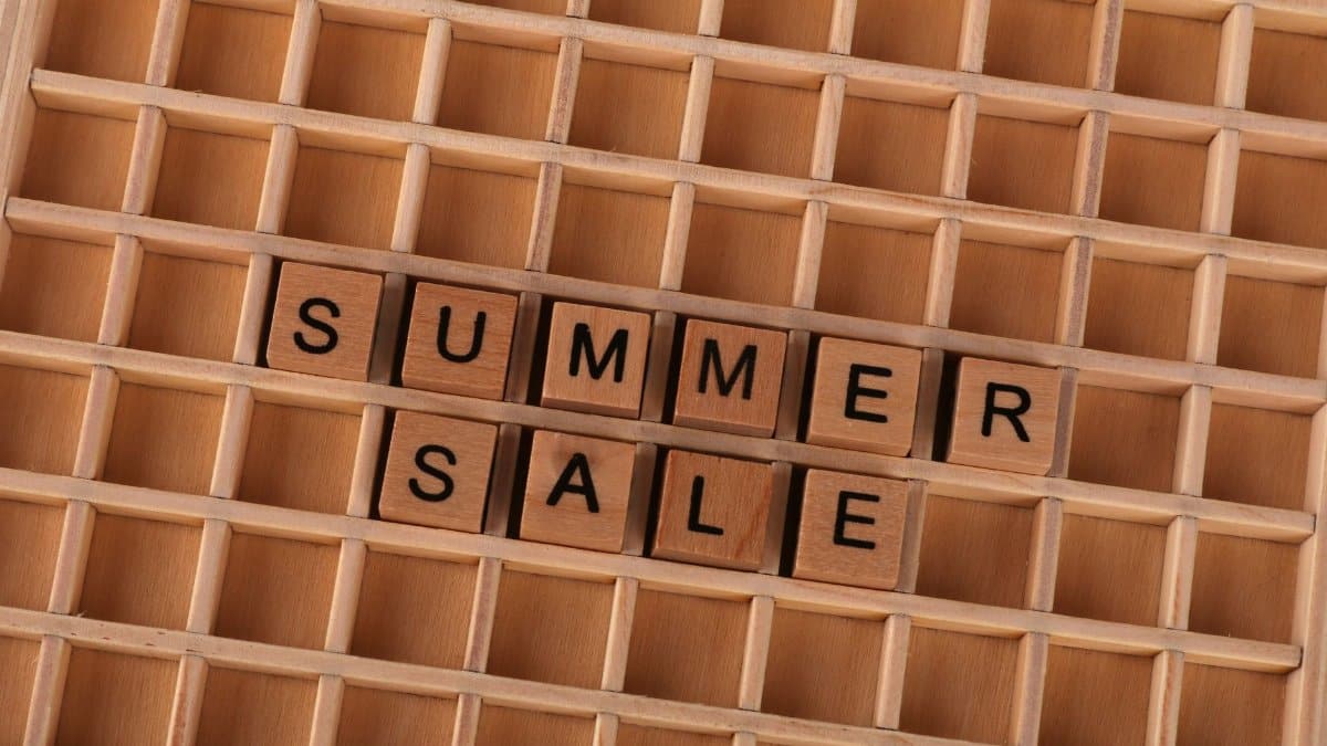 Wooden blocks arranged to spell 'Summer Sale' on a wooden grid background.