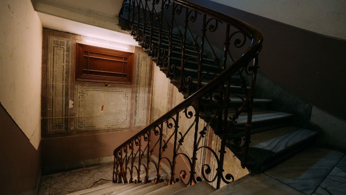 A classic interior staircase with intricate wrought iron railing and marble steps in moody lighting.