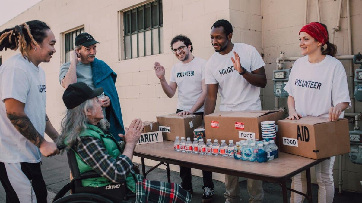 Group of volunteers providing food and aid to a person in wheelchair outdoors.