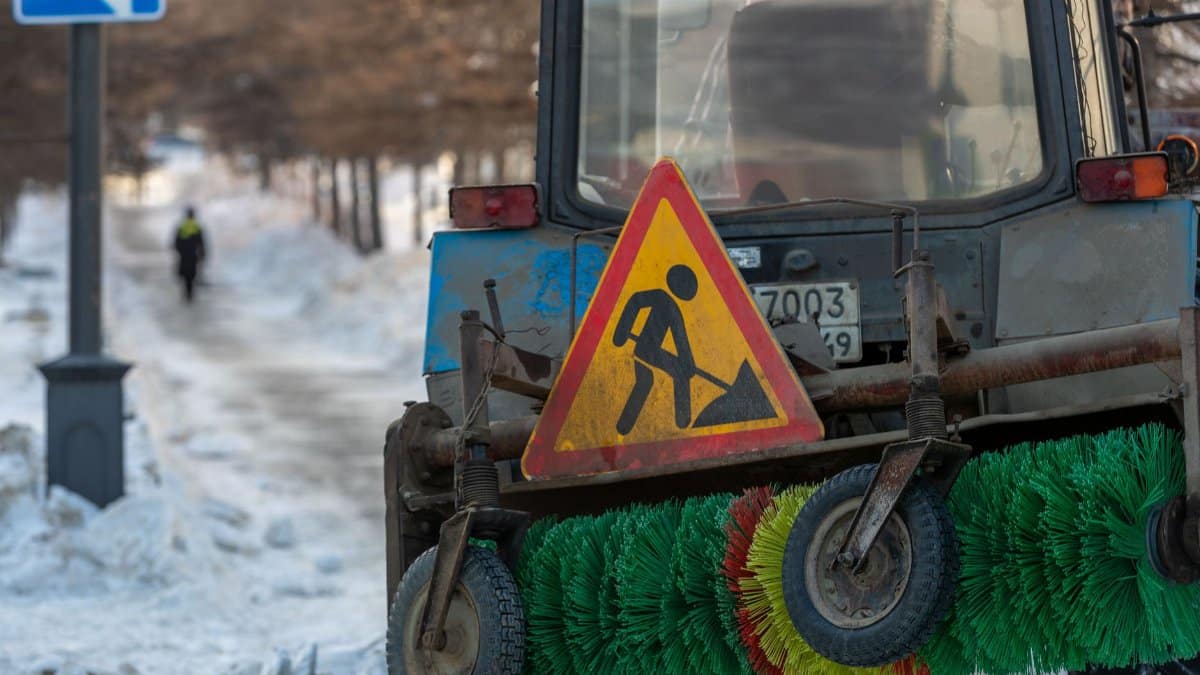 A snow tractor equipped for urban street cleaning clears a snowy path in the city.