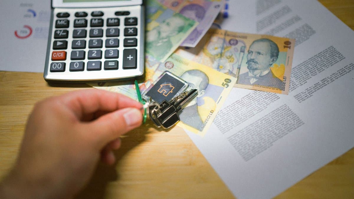 A hand holds keys next to Romanian currency, a calculator, and documents, symbolizing real estate transactions.