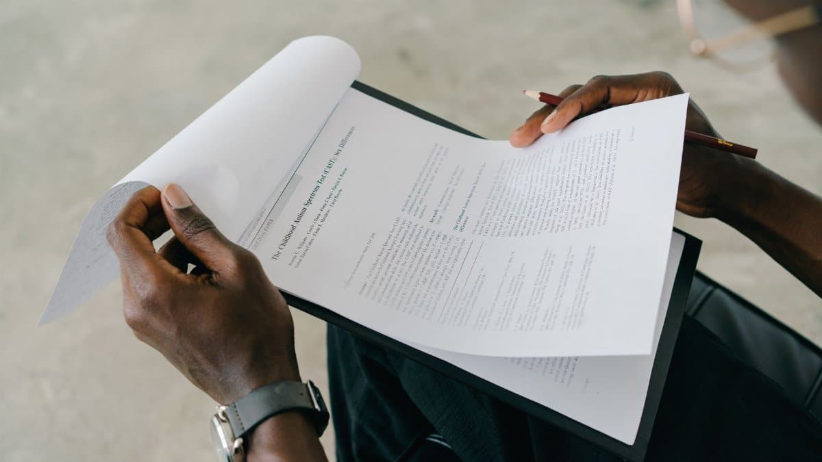 Hands holding and reviewing business documents with a pen, focusing on detailed paperwork.