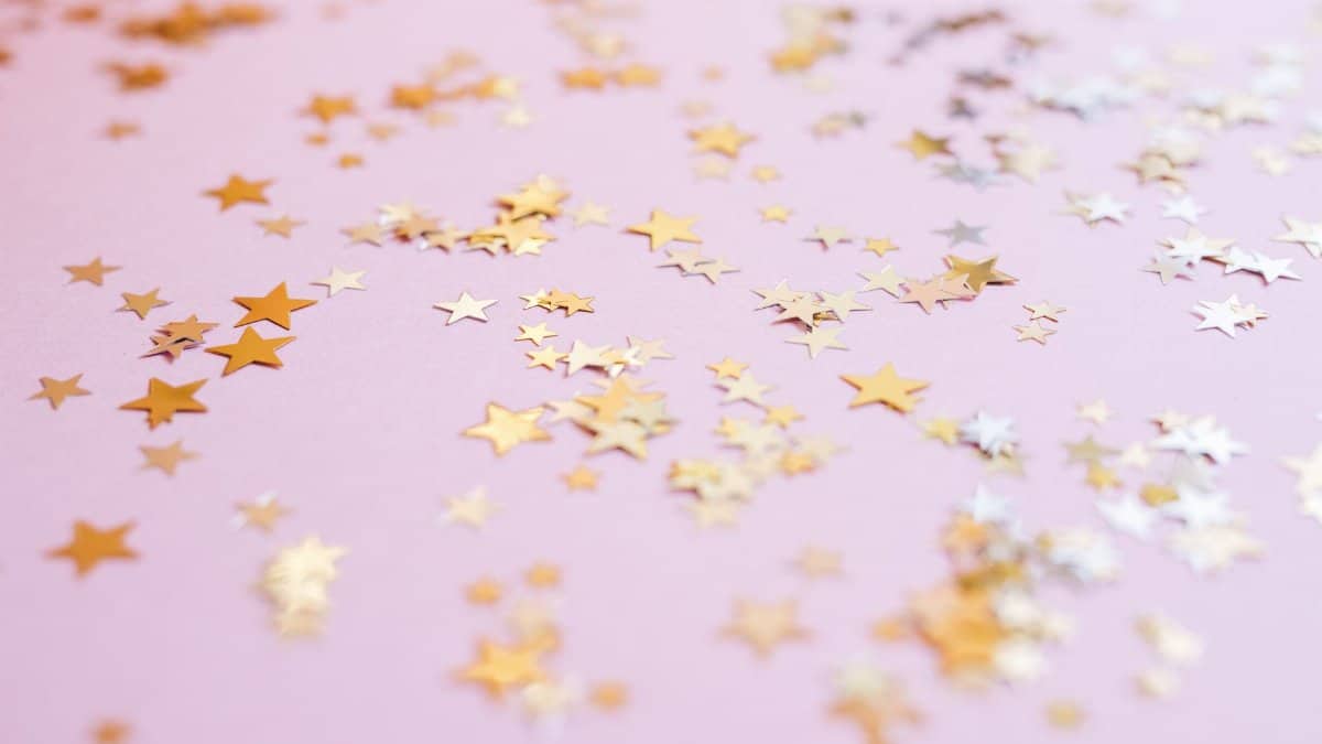 Scattered gold star confetti on a soft pink background for festive celebrations.
