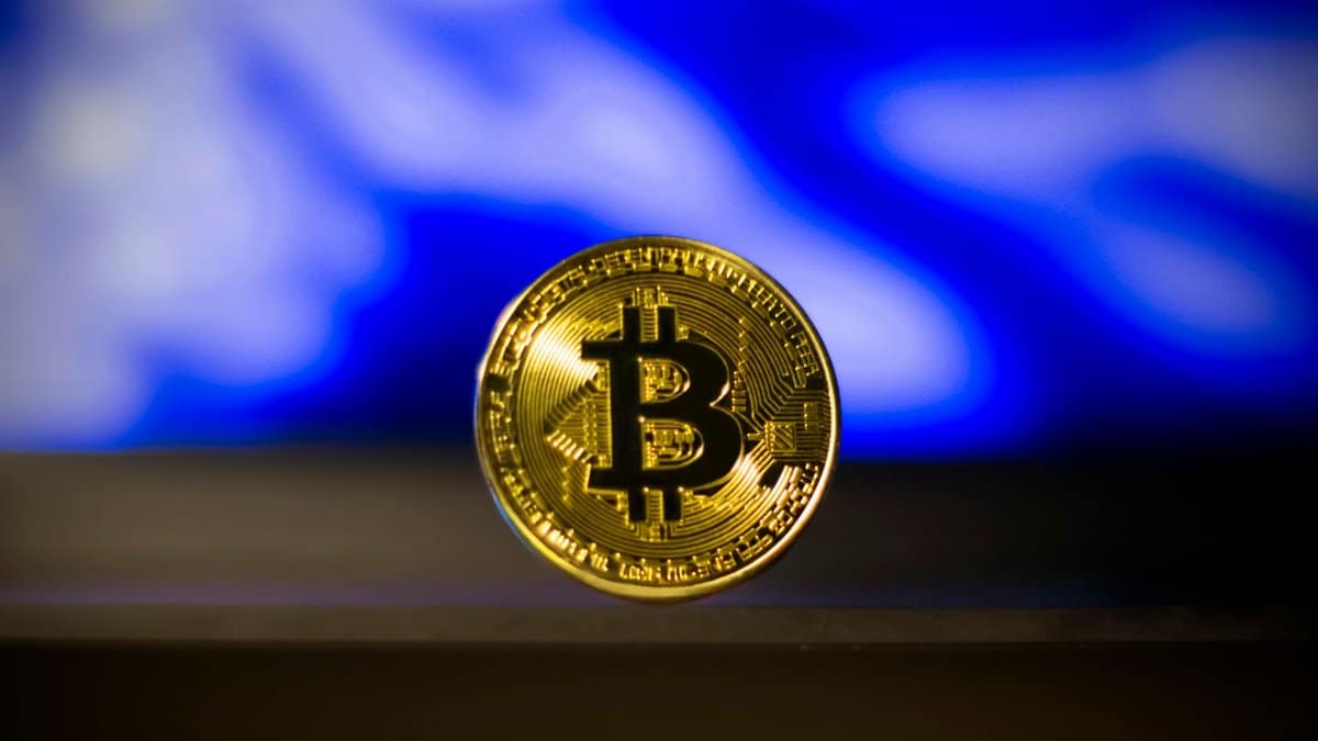Close-up of a golden Bitcoin coin with a blurred blue abstract background, symbolizes digital currency.