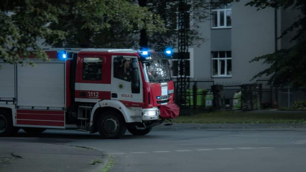 Red and white fire truck with flashing lights responding to an emergency in an urban area.