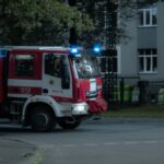 Red and white fire truck with flashing lights responding to an emergency in an urban area.